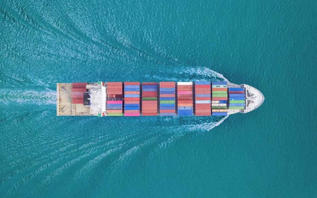 An aerial view of a colorful, loaded cargo ship moving across the ocean