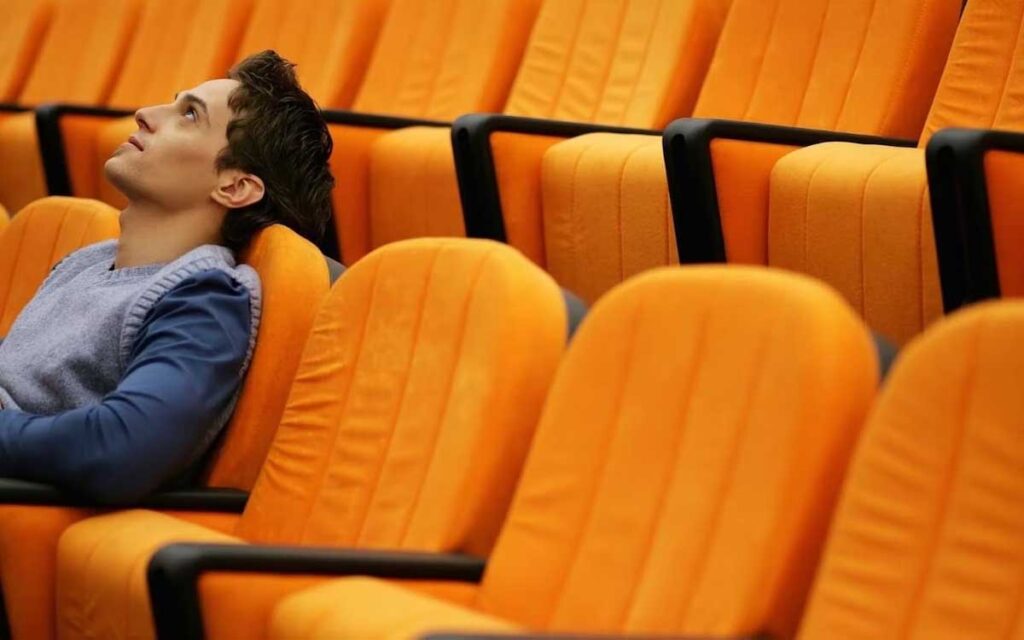 business analytics mba :A male college student sits in a lecture hall with orange chairs while looking up