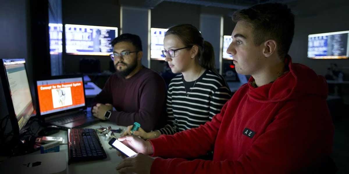Three Stevens students working together at a desktop in the computer lab