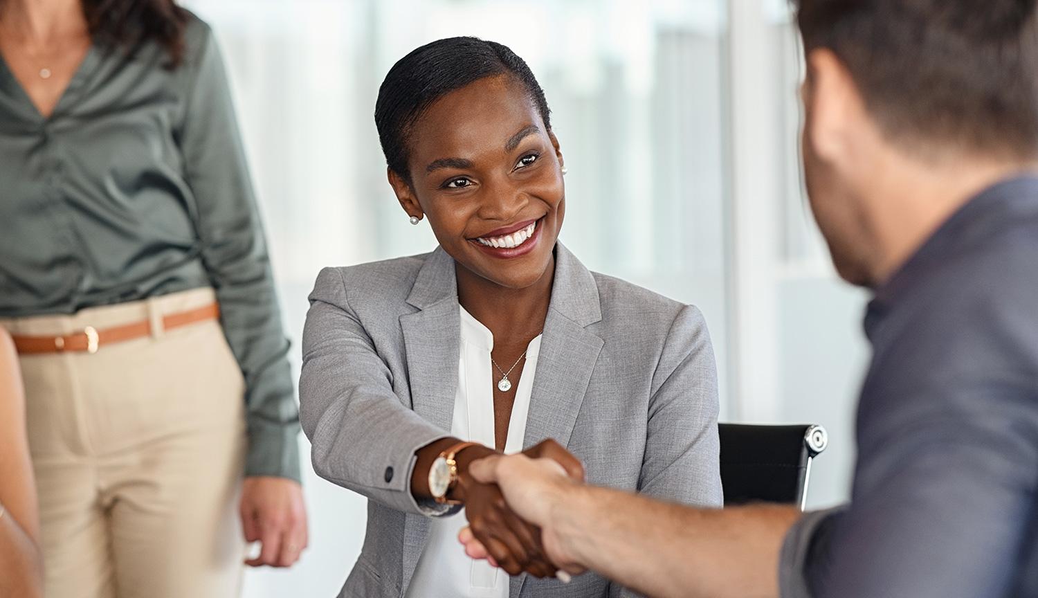 A professional woman smiling while shaking hands with a colleague in a business meeting.