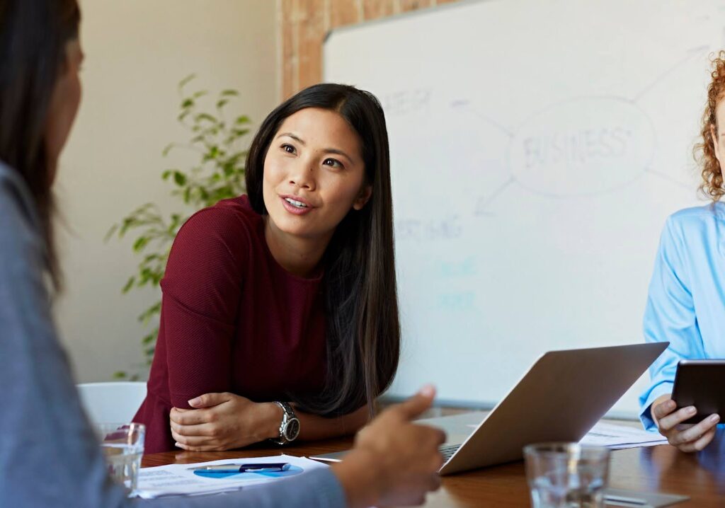 A business woman at a conference table discusses a project with peers.