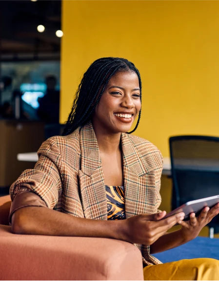 An Online MBA students sits in a comfortable chair while holding a tablet.